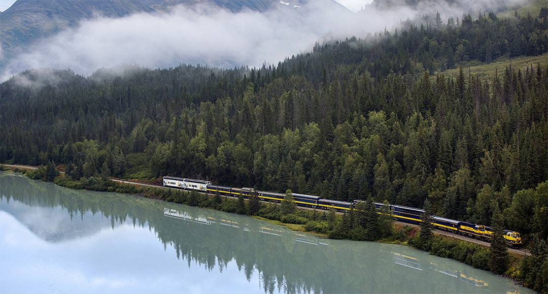 Train traveling along water and forest edge